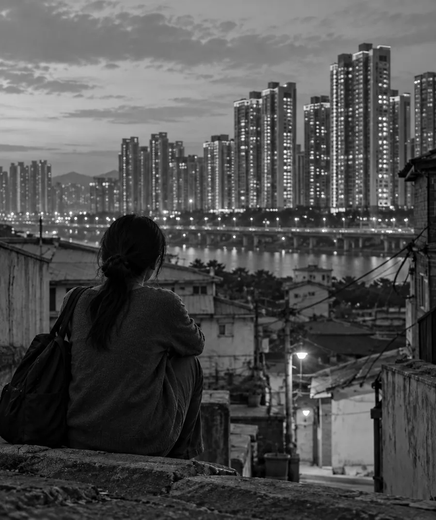 달동네 계단에 앉아 강 건너 아파트 불빛을 바라보는 사람의 뒷모습 (흑백)